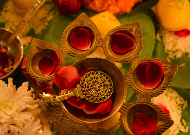 Top view of golden key with mandala head and rose petals on diya