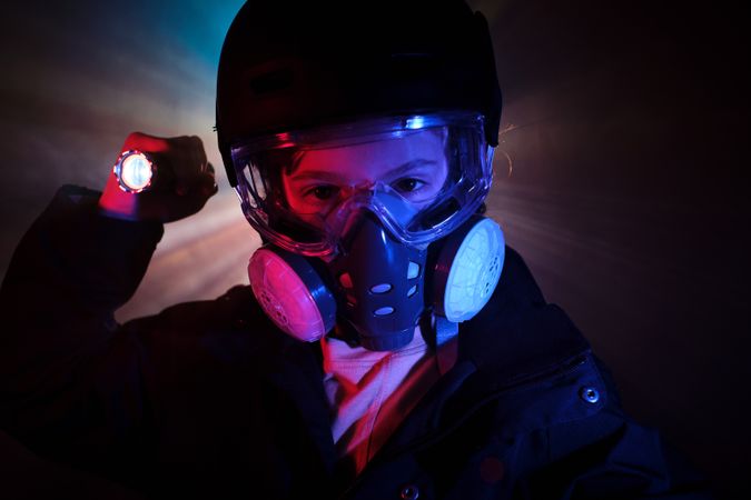 Boy in gas mask shining flashlight in dark studio