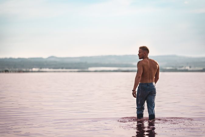 Undressed muscular man walking on shore of pink lake