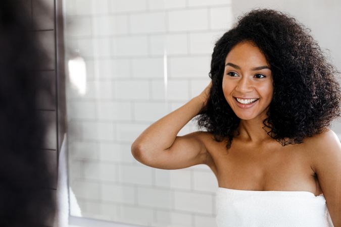 Smiling Black woman with curly hair looking in the mirror fixing her hair