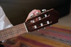 Crop person tuning acoustic guitar