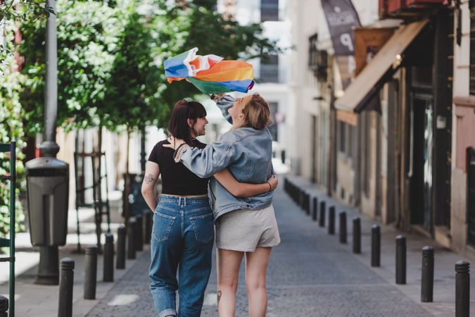 Lesbian couple with LGBT flag walking on street
