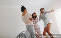Young women having fun singing karaoke standing on bed 5aoyAb