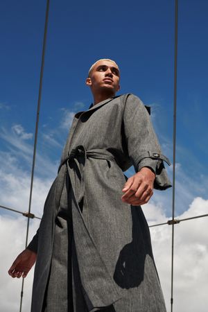 Stylish young man in belted gray coat against a blue sky
