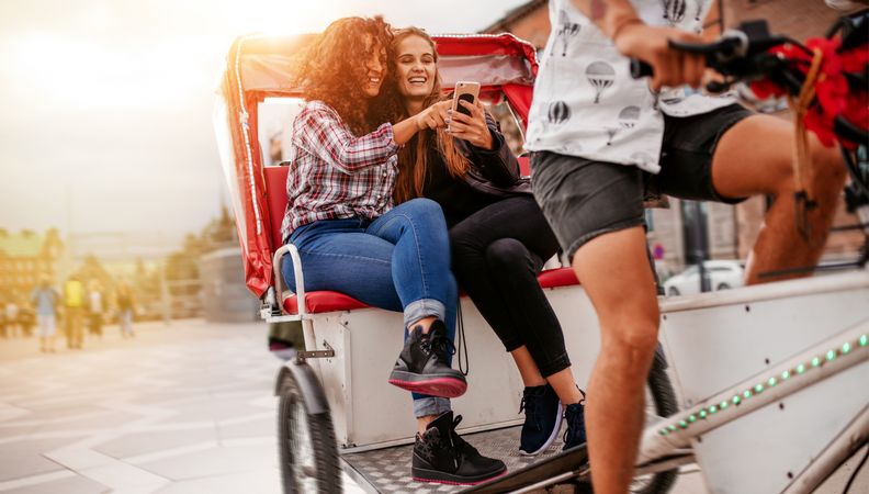 Female friends enjoying tricycle ride on road and using smart phone