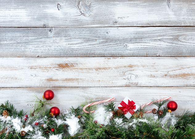 Snowy bottom border of Christmas evergreen branches with other holiday decorations on rustic wooden boards