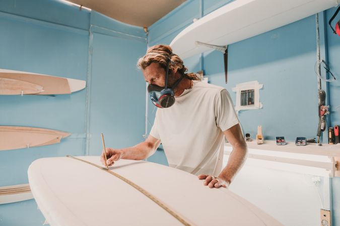 Man in respirator measuring surf board in workshop