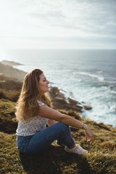Pensive woman sitting on grass and looking at seascape