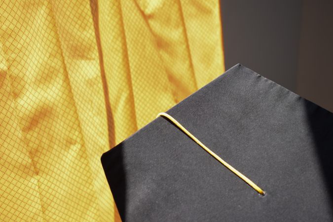 Top view of graduation cap with yellow tassel on yellow background