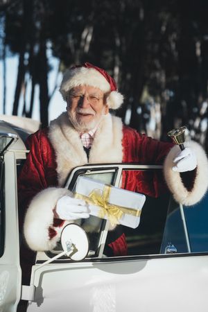 Cheerful Santa Claus in van with gift and bell