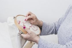 Woman's hand cross stitching pattern on a hoop against bright background