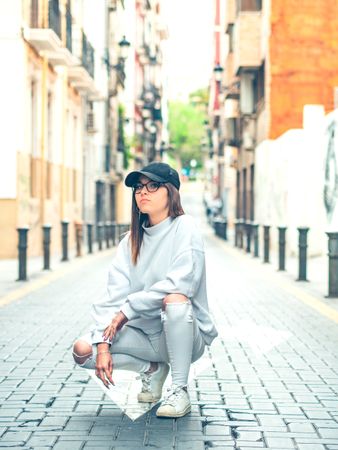 Young trendy woman sitting against street