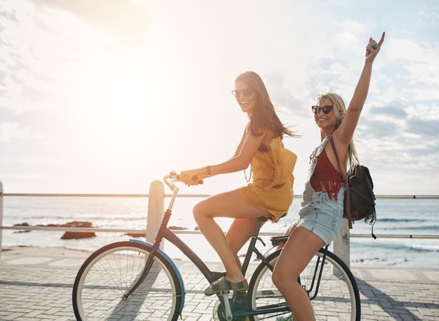 Two female friends on a bicycle at seaside promenade on a sunny day