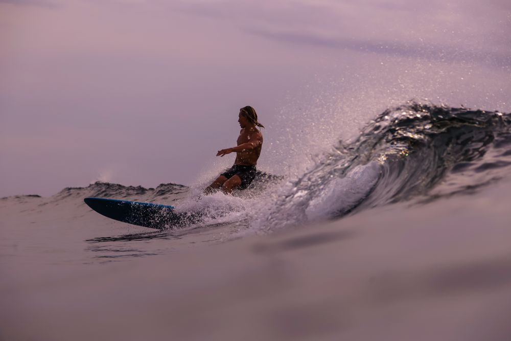 Man on surf board on waving water at sunset