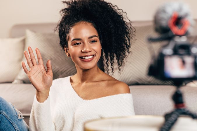 Smiling woman in her living room waving at a camera