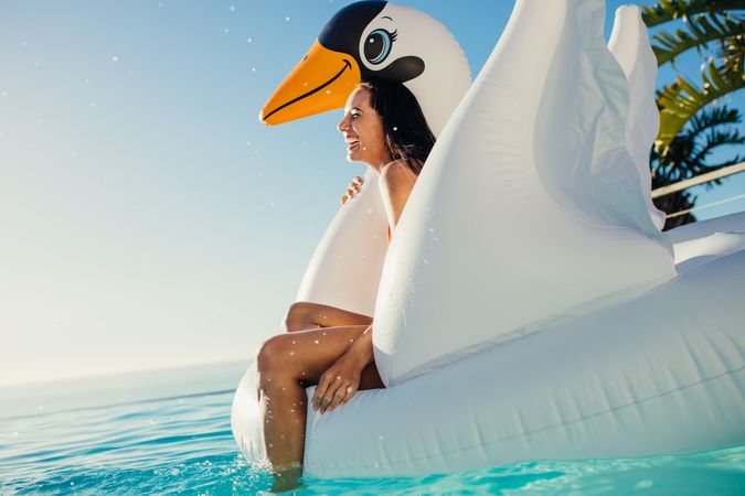 Cheerful young woman smiling while floating on inflatable swan