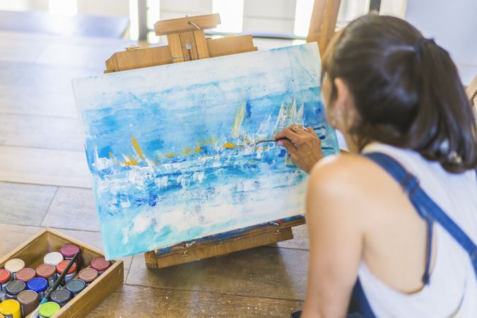 Woman artist painting on a canvas a blue abstract painting. Creative ywoman working on the floor in her art studio.