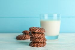 Stack of chocolate cookies with glass of milk on table against color background