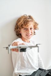 Cheerful cute preteen boy sitting with drone and remote control