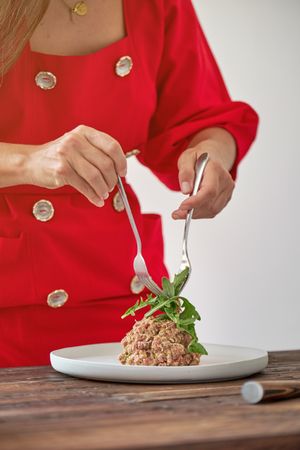 Crop woman decorating steak tartar with green leaves