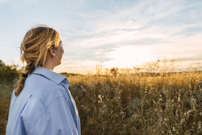 back view of a blonde woman portrait on a field during sunset