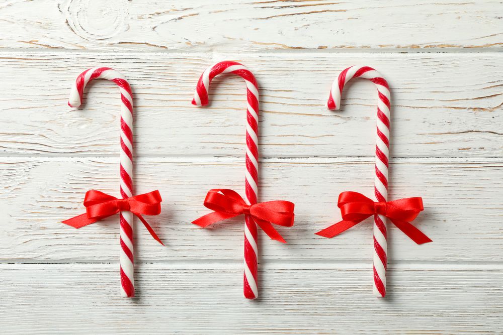 Sweet candy canes with bows on wooden background, space for text