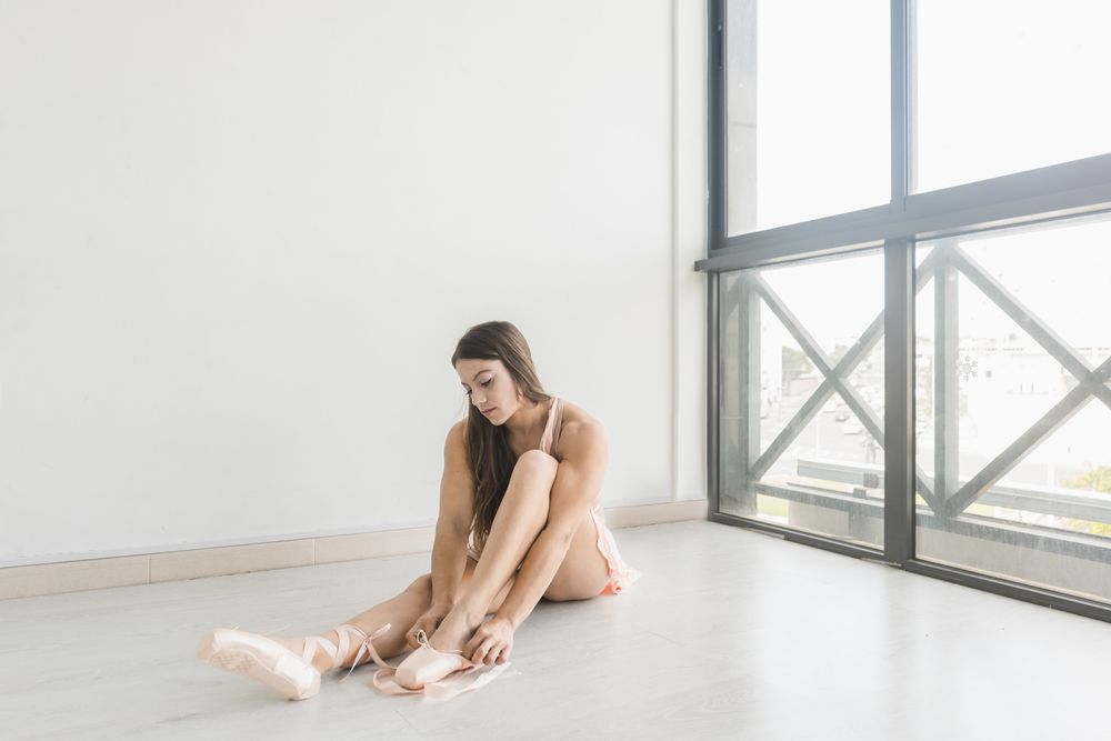 ballerina getting into ballet shoes in studio