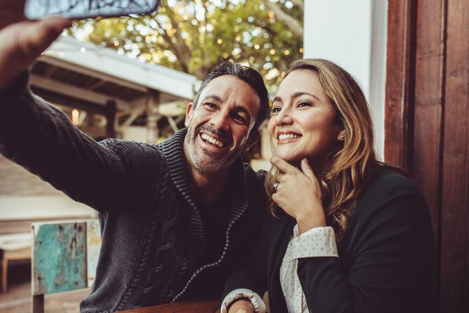 Smiling couple sitting at cafe taking selfie