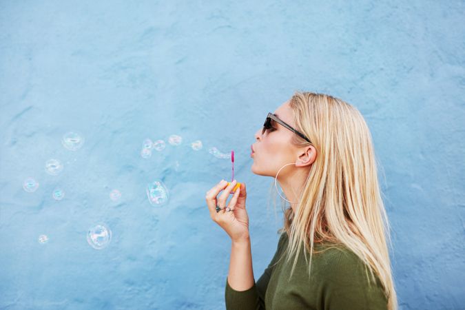 Profile of woman with long, blonde, straight hair blowing bubbles