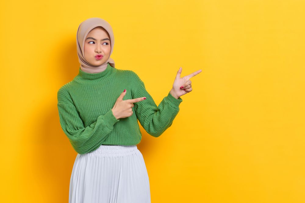 Pouting woman in headscarf pointing both her finger towards the side