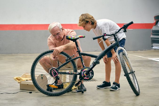 Older man pumping bicycle tire with attentive grandson
