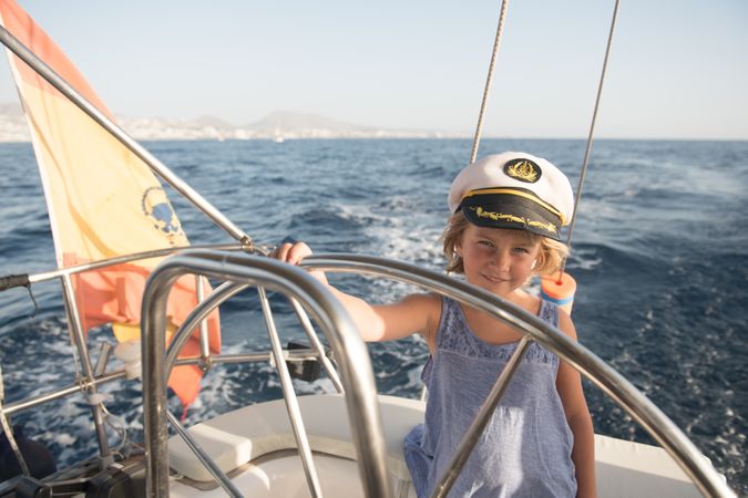 Smiling girl holding steering wheel on yacht on water