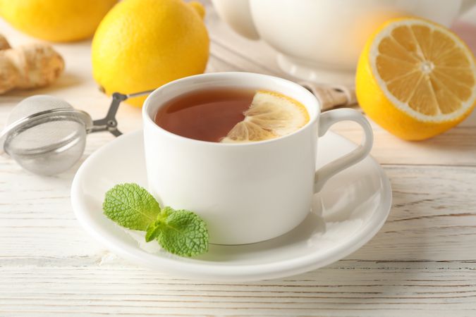 Cup of tea with lemon, mint, strainer, ginger and teapot on wooden background, close up