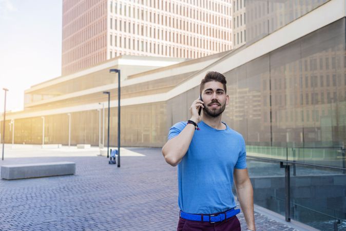 Portrait of man in blue t-shirt speaking on phone while walking outdoors