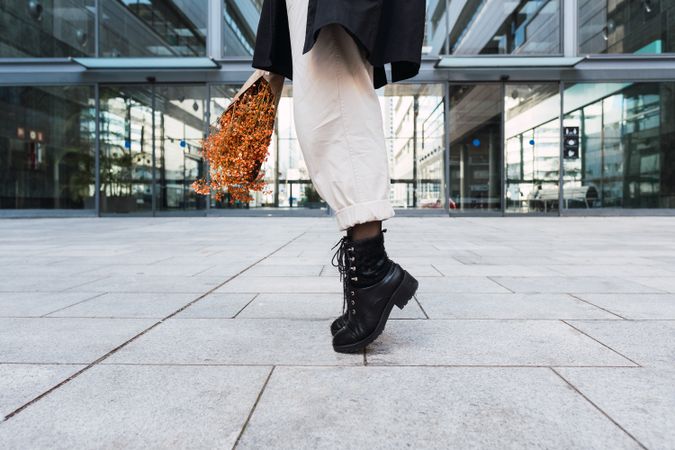 Crop woman with bouquet tiptoeing on street
