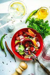 Top view of colorful healthy raw vegetable salad served in red bowl with water to drink