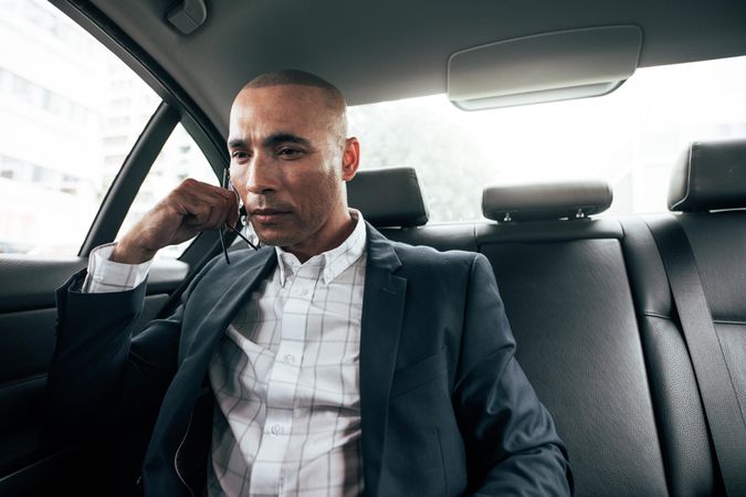 Man holding eyeglasses in hand sitting in his sedan on back seat