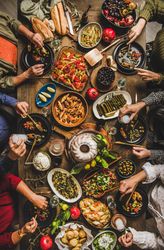 Group of people at wooden table with meze feast, cake and white aperitif