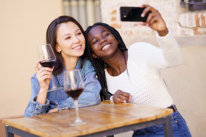 Female friends at a restaurant with glasses of red wine taking a self portrait