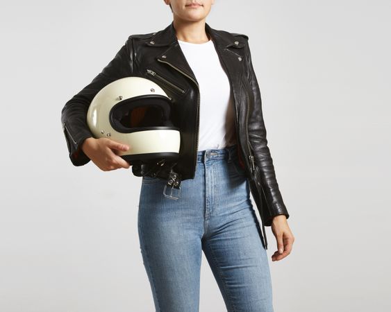 Woman in dark leather jacket with light t-shirt holding motorcycle helmet