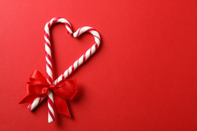 Sweet candy canes with bow on red background, space for text