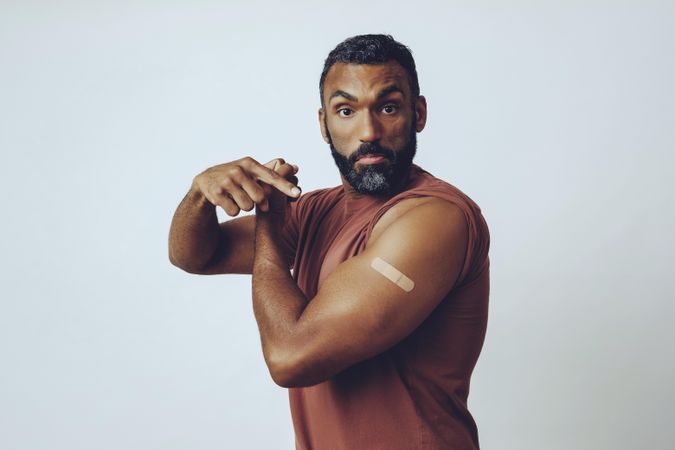 Proud man flexing arm and pointing at vaccination with copy space