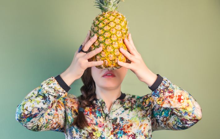 Woman holding pineapple in front of face