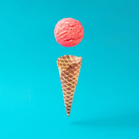 Waffle cone with separated scoop of pink ice cream on bright blue background
