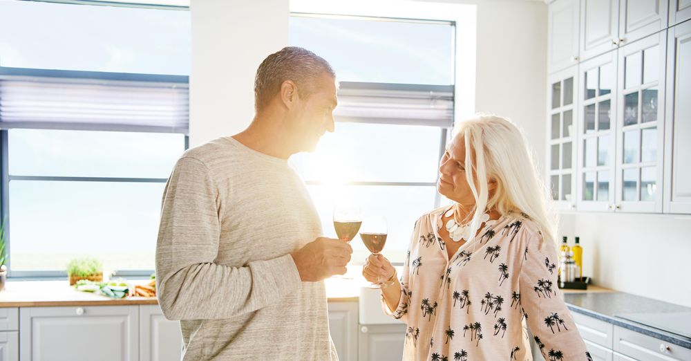 Mature couple toasting glasses of red wine in a bright kitchen