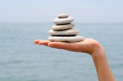 Side view of hand with small pile of rocks with seaside view in background