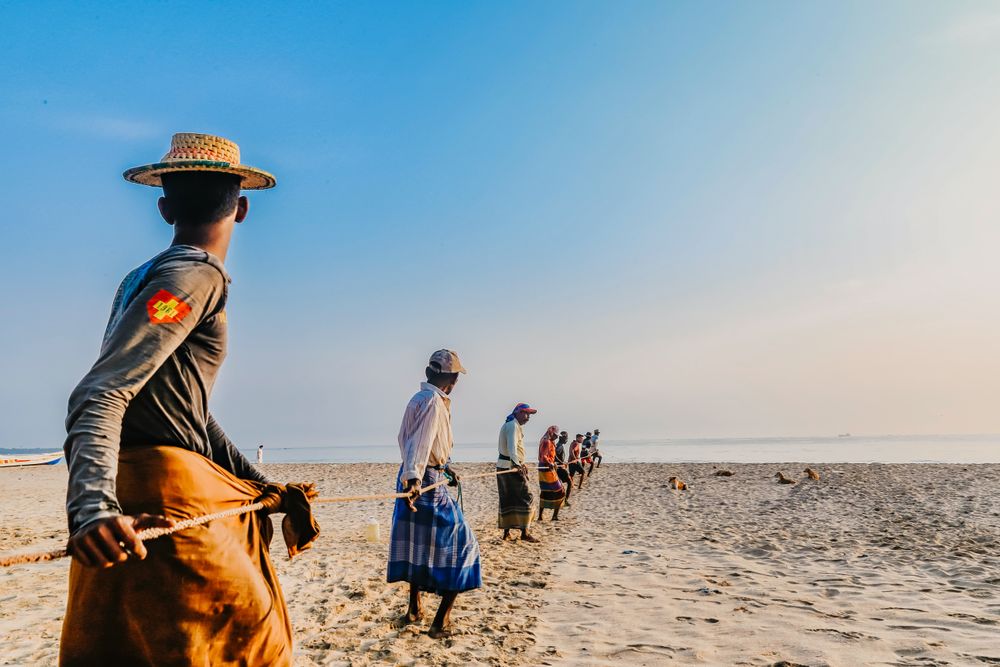Back view of African men holding pulling a rope on the beach