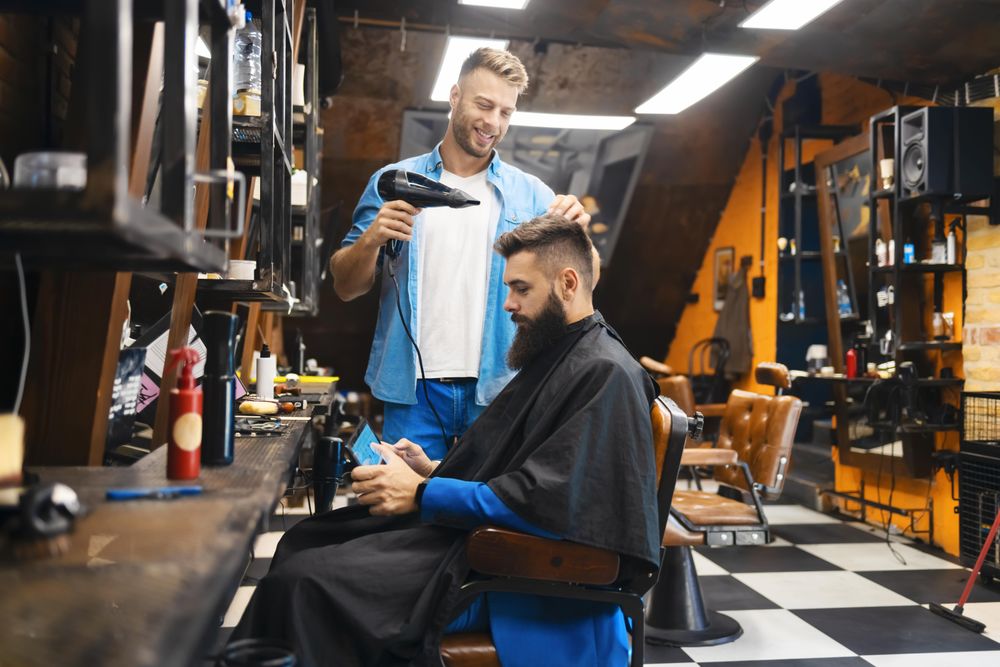 Man looking at his phone while having his hair blowdried