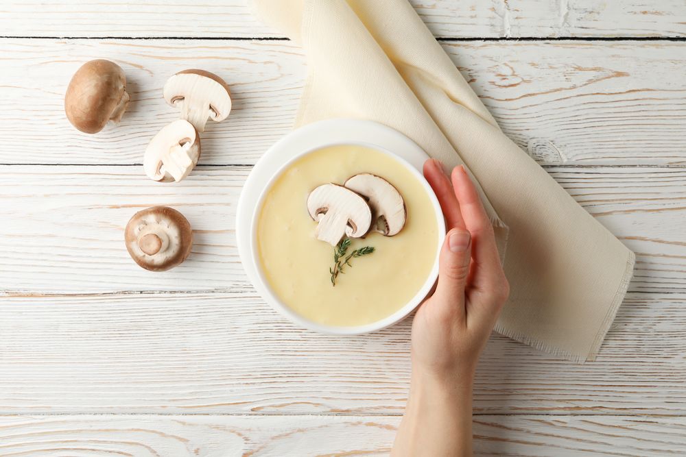 Hand holding a bowl of of creamy soup on table