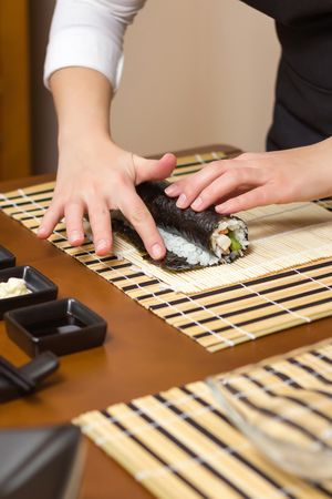 Woman hand moistening with water a edge of Japanese sushi to close the roll